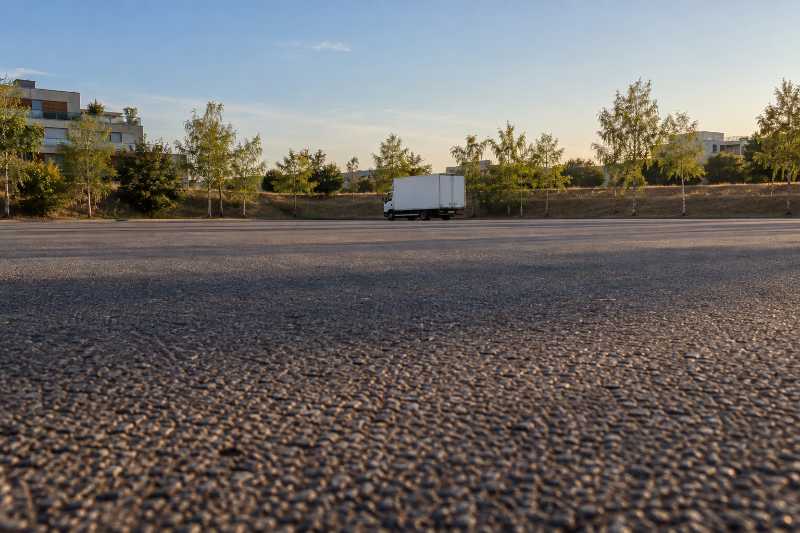 Vaste parking vide en enrobé, un seul camion de déménagement arrêté au fond