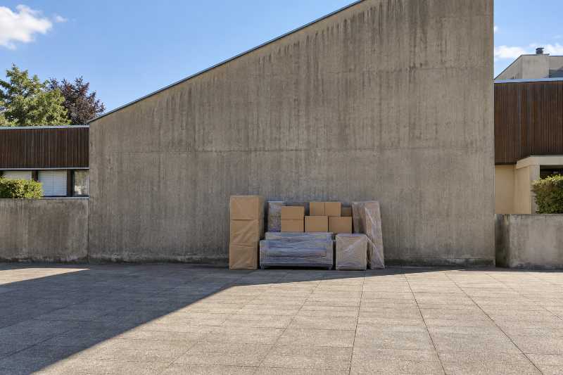 Mobilier emballé et cartons empilés au pied d'un mur pignon aveugle en béton